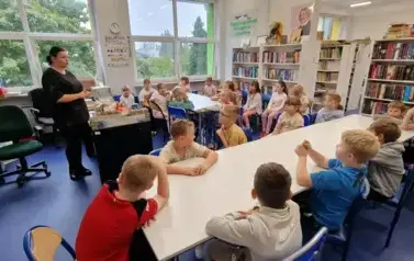 uczniowie siedzą przy stolikach w bibliotece szkolnej