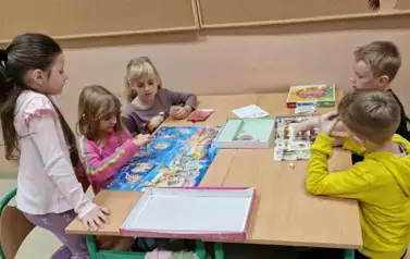dziewczynki i chłopcy wsp&oacute;lnie grają przy stoliku
