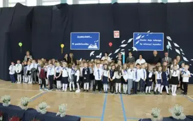 uczniowie klas pierwszych na tle dekoracji wraz z zaproszonymi gośćmi i wychowawczyniami klas pierwszych