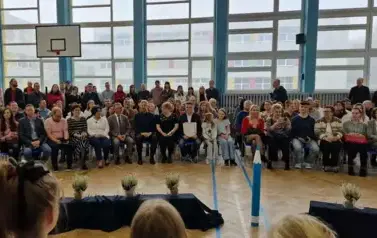 grupa os&oacute;b siedząca na widowni, wśr&oacute;d nich Prezydent Miasta, Naczelnik wydziału, Panie dyrektorki szkoły oraz rodzice i dziadkowie
