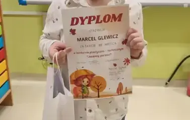 Marcel stoi i pozuje z dyplomem i nagrodą