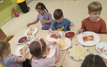 dzieci na przy stole nakładają skałdniki na pizzę