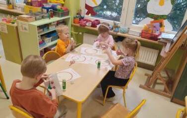 dzieci siedzą przy stoliku i wycinają elementy do karty pracy