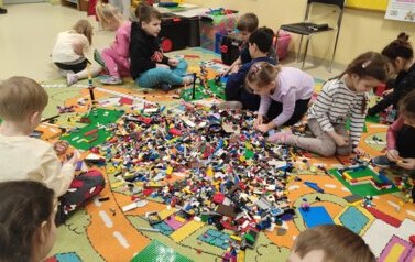 dzieci siedzą na dywanie i budują z  klock&oacute;w lego