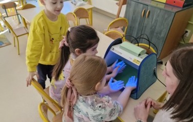 przedszkolaki obserwują swoje ręce pod lampą UV