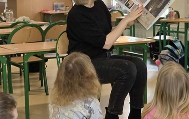 Zdjęcie przedstawia nauczycielkę czytająca na głos książkę pod tytułem &bdquo;Słoiki pełne szczęścia Deborah Marcero