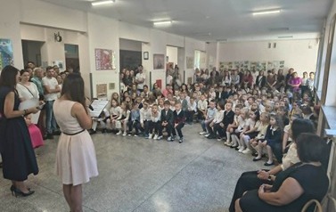 nauczycielki prowadzące uroczystość rozpoczęcia roku szkolnego stojące przed zgromadzonymi w holu szkoły dziećmi i rodzicami