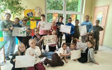 Grupa dzieci w sali lekcyjnej prezentuje duży plakat dotyczący przeciwdziałania przemocy r&oacute;wieśniczej