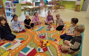 grupa siedzi na dywanie i por&oacute;wnuje jabłka pod względem koloru, wielkości