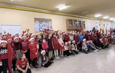 Grupa uczni&oacute;w zgromadzonych na szkolnym korytarzu w Dużej 8 w czapkach Świętego Mikołaja i opaskach z porożem renifera 