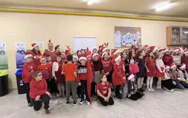 Grupa uczni&oacute;w zgromadzonych na szkolnym korytarzu w Dużej 8 w czapkach Świętego Mikołaja i opaskach z porożem renifera