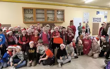 Grupa uczni&oacute;w zgromadzonych na szkolnym korytarzu w Dużej 8 w czapkach Świętego Mikołaja i opaskach z porożem renifera