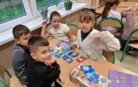 dziewczynki i chłopcy siedzą przy stoliku i grają w grę planszową