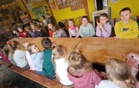 uczniowie klas pierwszych siedzą prze wsp&oacute;lnym stole i słuchają opowieści o pszczołach