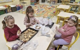 Dzieci obsypują upieczone ciasteczka pukrem pudrem i pakują je do woreczk&oacute;w