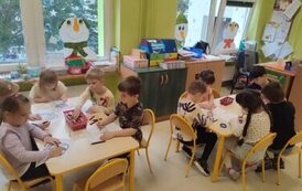 przedszkolaki siedzą przy stolikach i malują wymyślonego przez siebie ludzika Lego