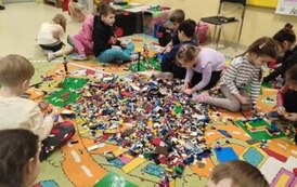 dzieci siedzą na dywanie i budują z  klock&oacute;w lego