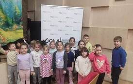 grupa przedszkolna stoi przed sceną w sali muzycznej i pozuje do zdjęcia