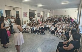 nauczycielki prowadzące uroczystość rozpoczęcia roku szkolnego stojące przed zgromadzonymi w holu szkoły dziećmi i rodzicami