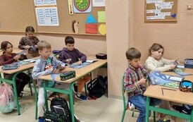 Uczniowie siedzą w ławkach szkolnych i wycinają maski superbohater&oacute;w