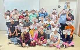 Grupa uczni&oacute;w siedzi i stoi w sali, prezentując wykonane przez siebie kolorowe papierowe okulary. Na okularach znajdują się wzory, napisy i ilustracje związane z tematyką Tygodnia Przeciwdziałania Przemocy R&oacute;wieśniczej.