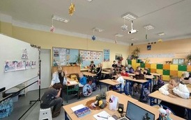 Uczniowie uczestniczą w zajęciach w sali lekcyjnej. Na tablicy widoczne są materiały dotyczące bezpieczeństwa.
