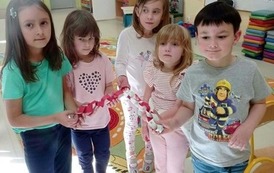 Pięcioro dzieci w sali przedszkolnej trzyma wykonany z papierowych ogniw &bdquo;łańcuch przyjaźni&rdquo;