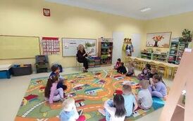 przedszkolaki siedzą w kole na dywanie i słuchają książki czytanej przez Panią Olę z biblioteki