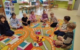 grupa siedzi na dywanie i por&oacute;wnuje jabłka pod względem koloru, wielkości