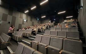 Prelekcja w kinie w ramach programu &bdquo;Młode Horyzonty&rdquo;. W sali kinowej siedzą uczniowie klas 3c i 3d. Dzieci zajmują miejsca na szarych, tapicerowanych fotelach ustawionych w rzędach na schodkowo wznoszącej się widowni