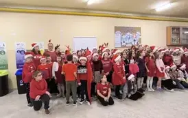 Grupa uczni&oacute;w zgromadzonych na szkolnym korytarzu w Dużej 8 w czapkach Świętego Mikołaja i opaskach z porożem renifera