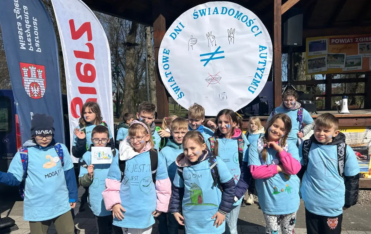 uczniowie pozujący do pamiątkowego zdjęcia przy logo obchodów Światowego Dnia Świadomości Autyzmu