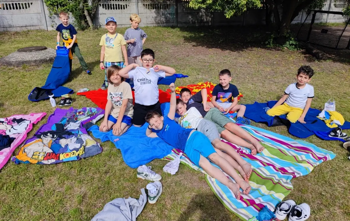Uśmiechające się dzieci, siedzące na kocach na boisku szkolnym 