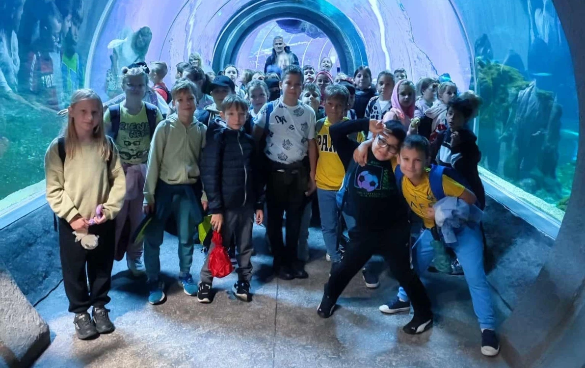 Grupa dzieci pozująca do zdjęcia na tle błękitnego oceanarium pełnego egzotycznych ryb