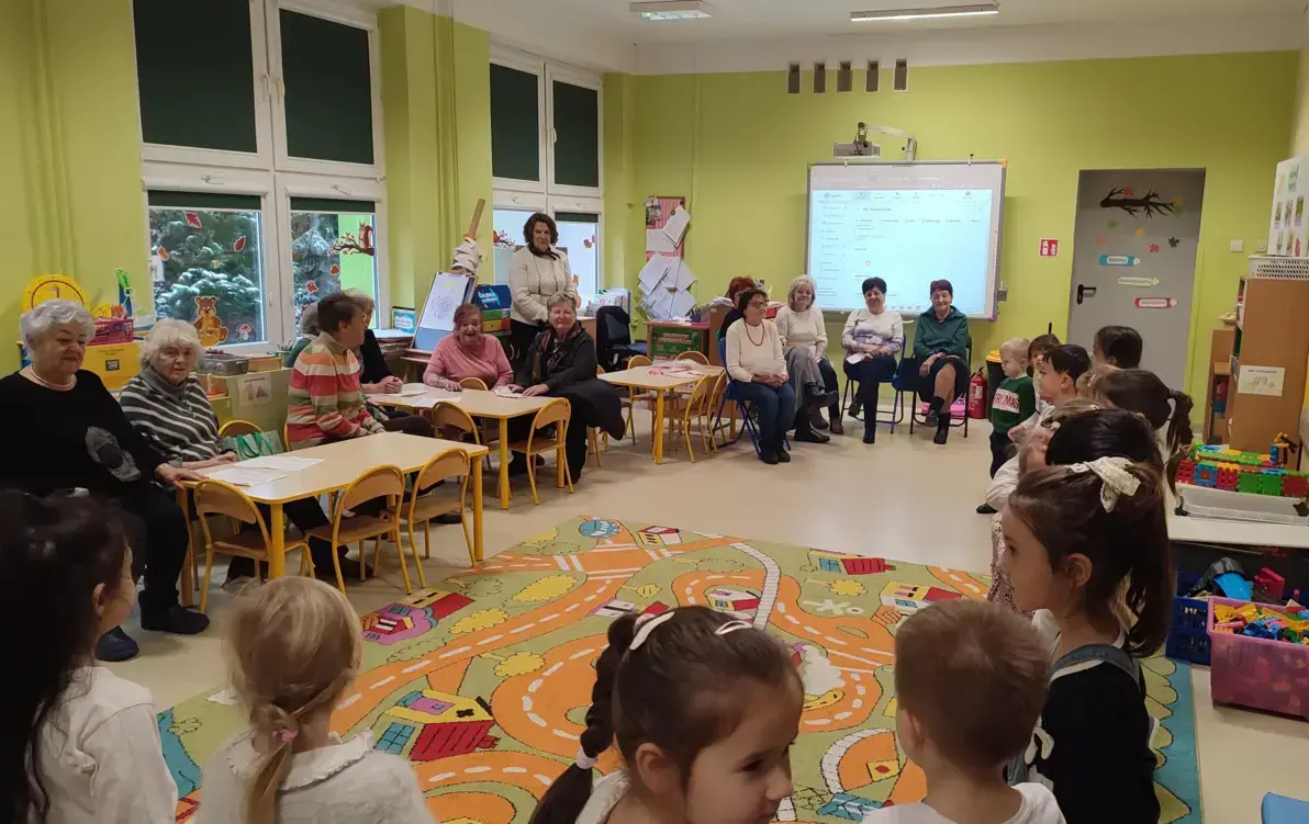 dzieci śpiewają piosenkę, seniorzy w sali ich słuchają