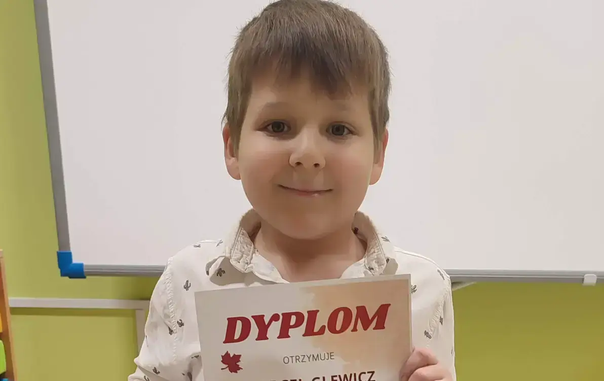Marcel stoi i pozuje z dyplomem i nagrodą