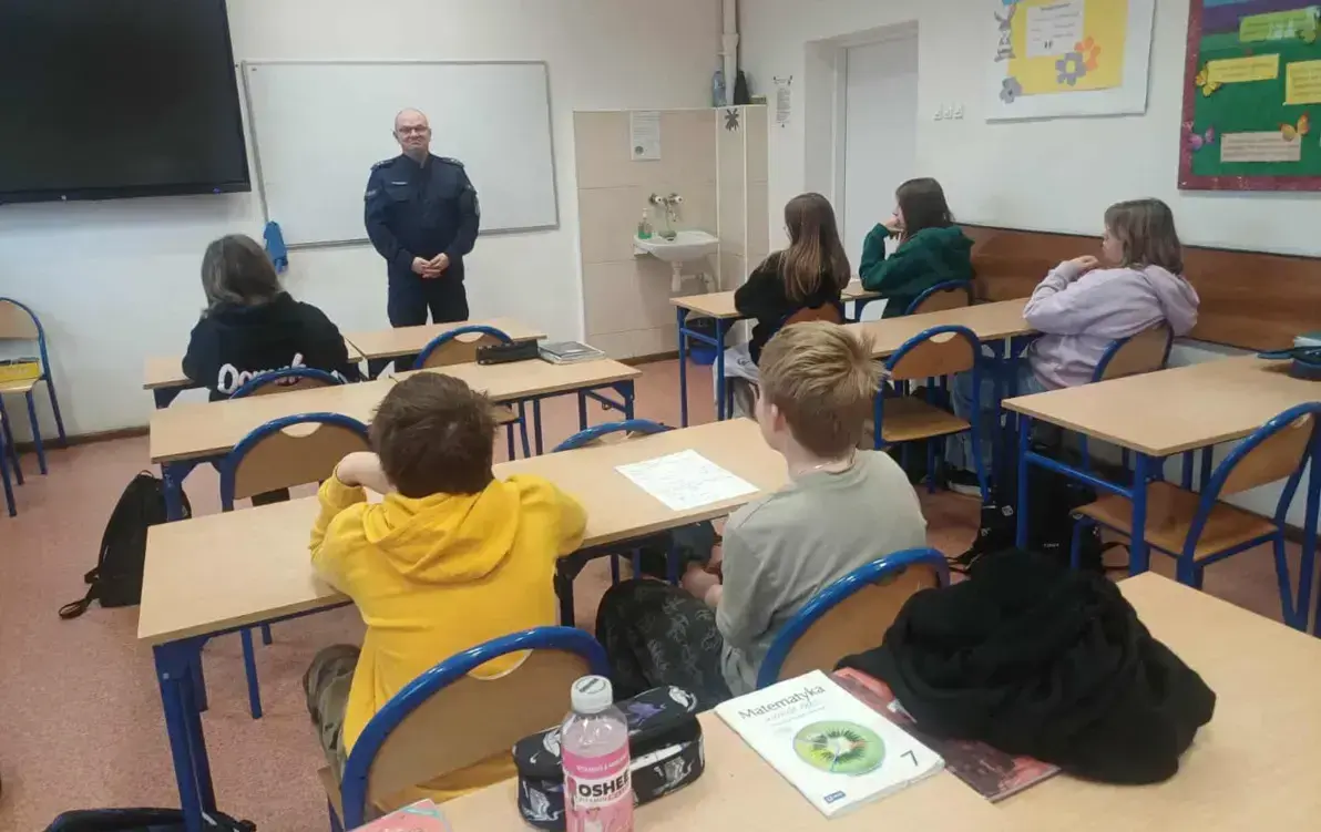 Uczniowie siedzą w ławka szkolnych podczas zajęć z policjantem rozmawiają na temat czym jest hejt, jak wygląda przemoc słowna w Internecie.