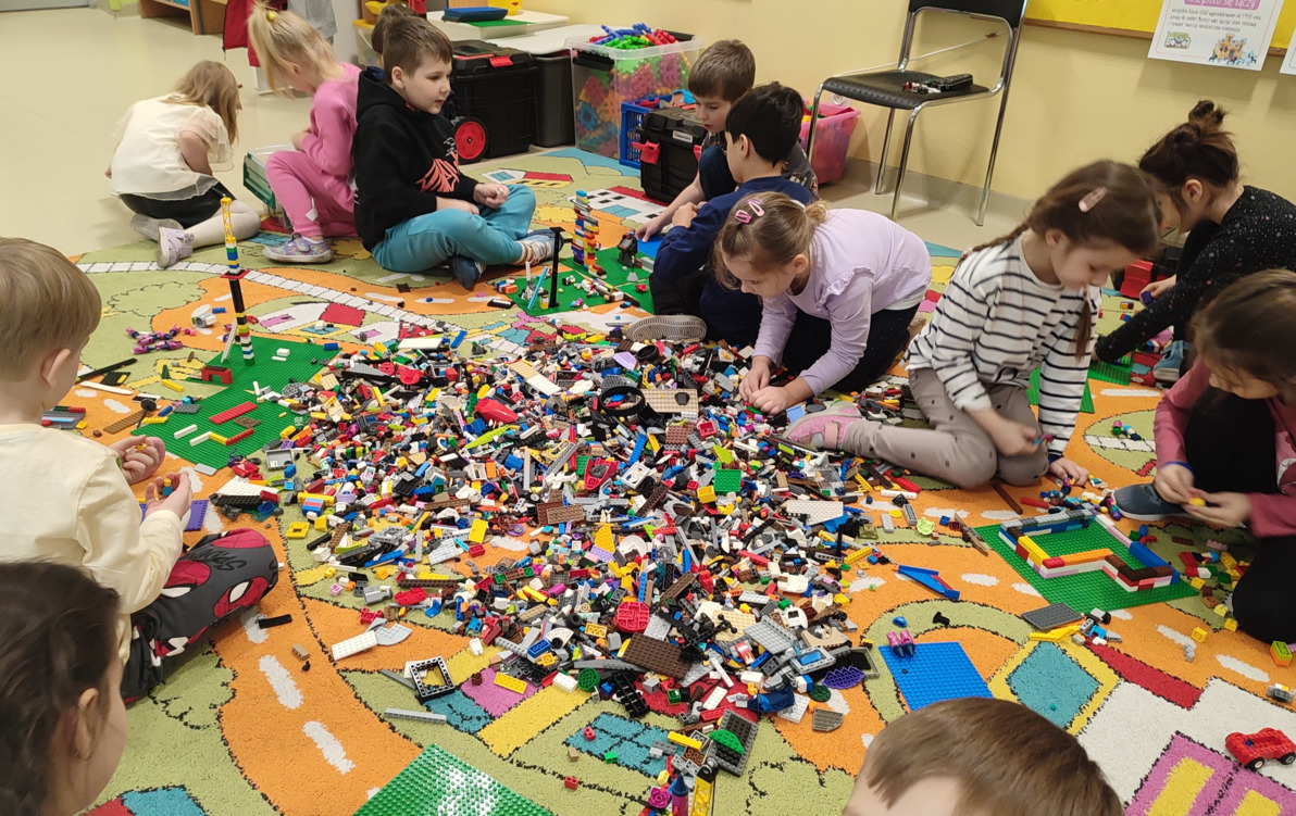 dzieci siedzą na dywanie i budują z  klocków lego