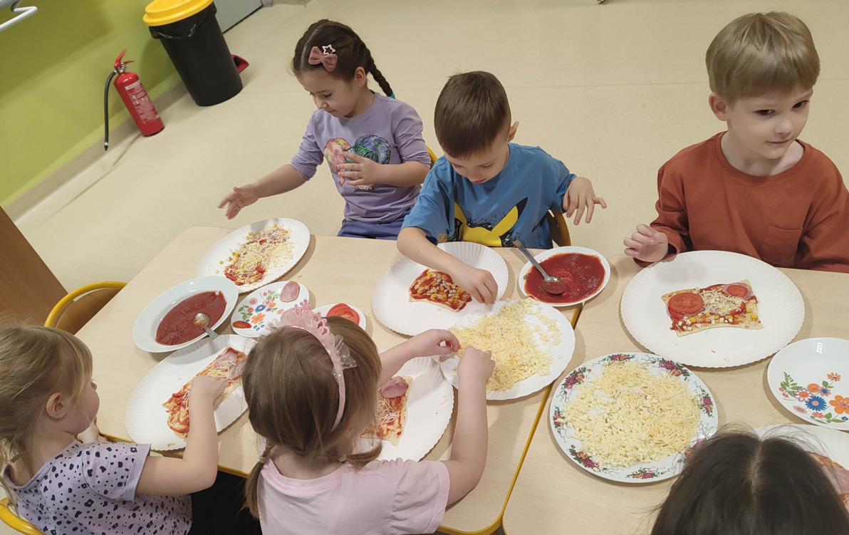 dzieci na przy stole nakładają skałdniki na pizzę
