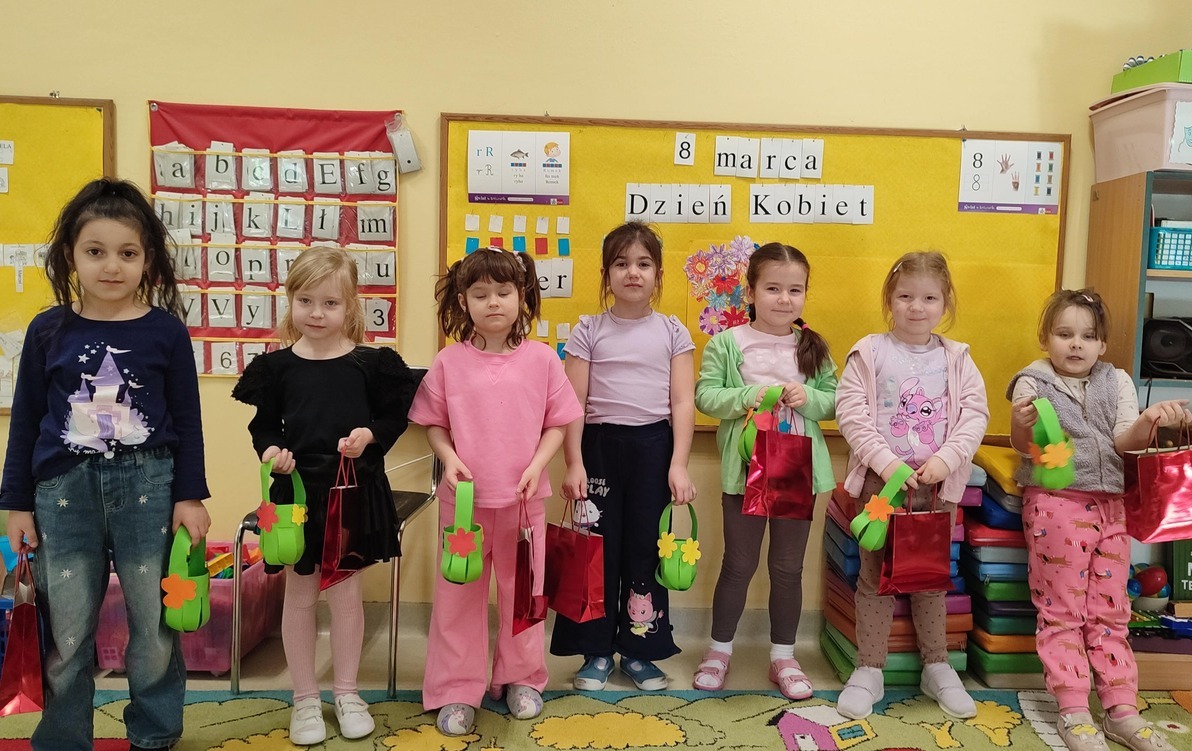 grupa dziewczynek pozuje na tle tablicy z prezentami z okazji dnia kobiet