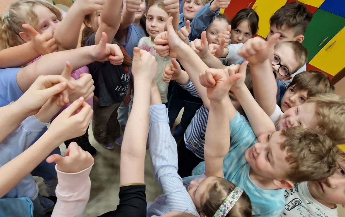 uczniowie stoją w grupe z podniesionym do góry kciukiem