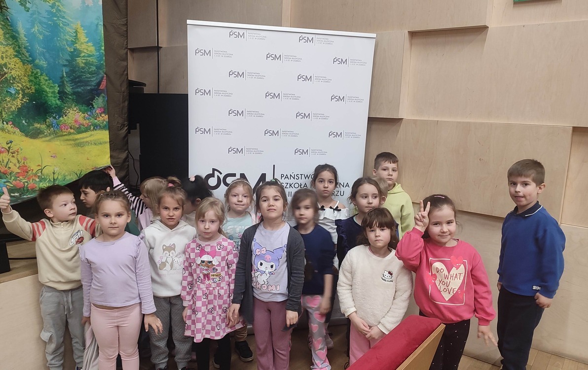 grupa przedszkolna stoi przed sceną w sali muzycznej i pozuje do zdjęcia