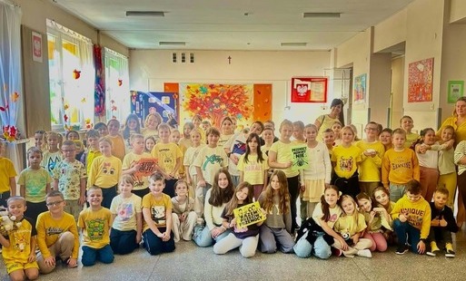 Duża grupa dzieci i nauczycieli na szkolnym korytarzu. Uczniowie trzymają plakaty i materiały związane z przeciwdziałaniem przemocy