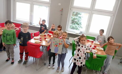 grupa przedszkolna stoi na stołówce z laurką