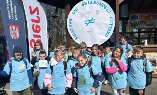 uczniowie pozujący do pamiątkowego zdjęcia przy logo obchodów Światowego Dnia Świadomości Autyzmu