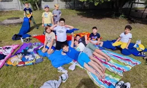 Uśmiechające się dzieci, siedzące na kocach na boisku szkolnym 