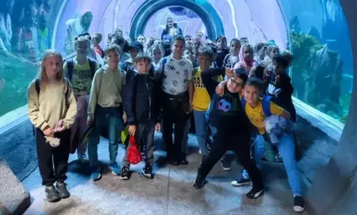 Grupa dzieci pozująca do zdjęcia na tle błękitnego oceanarium pełnego egzotycznych ryb