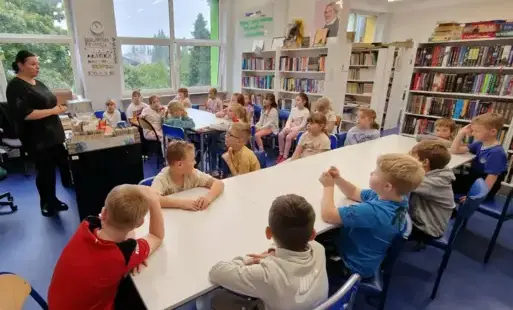 uczniowie siedzą przy stolikach w bibliotece szkolnej