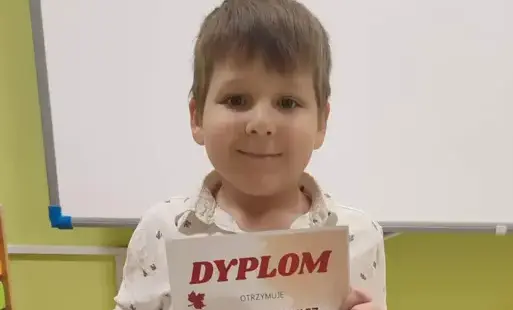 Marcel stoi i pozuje z dyplomem i nagrodą