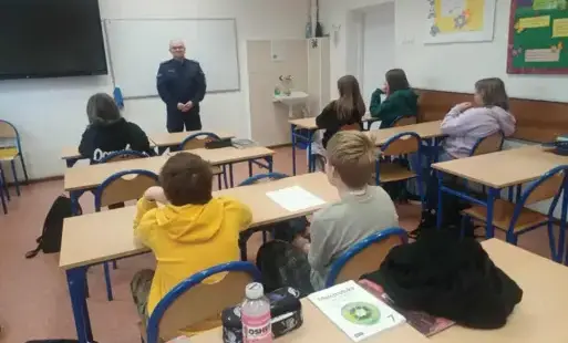 Uczniowie siedzą w ławka szkolnych podczas zajęć z policjantem rozmawiają na temat czym jest hejt, jak wygląda przemoc słowna w Internecie.